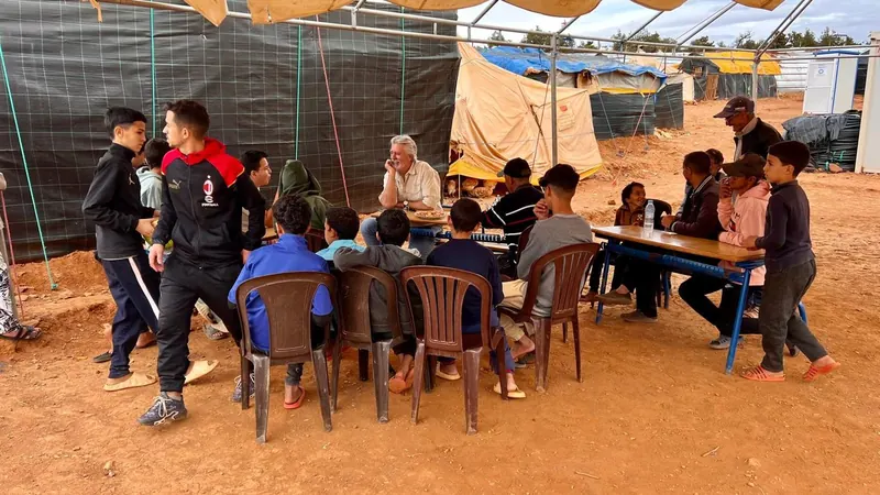 Children seated at tables inside a tented classroom shelter