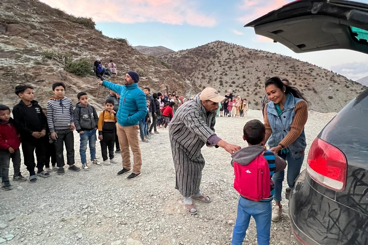 A School Aid team member and a local man handing a backpack to a child at dusk in the High Atlas