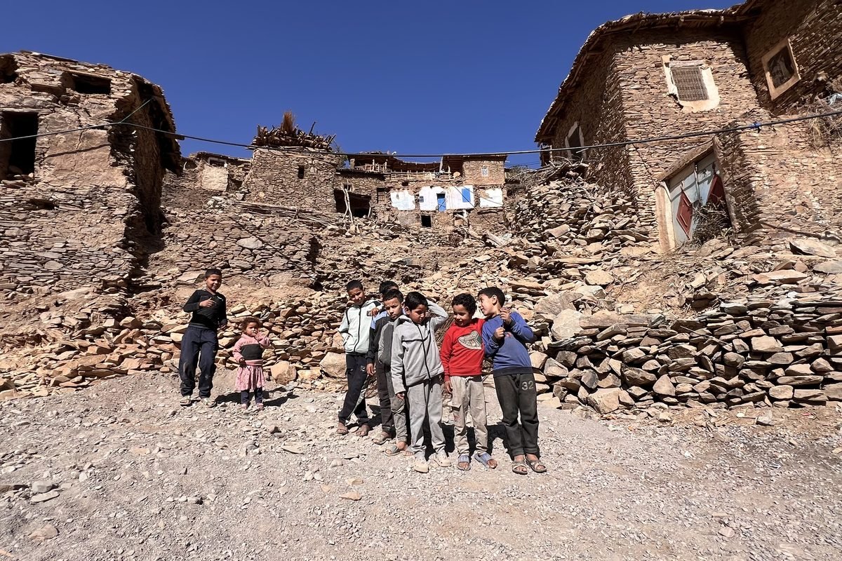 Children standing in front of an earthquake-damaged village in Morocco’s High Atlas